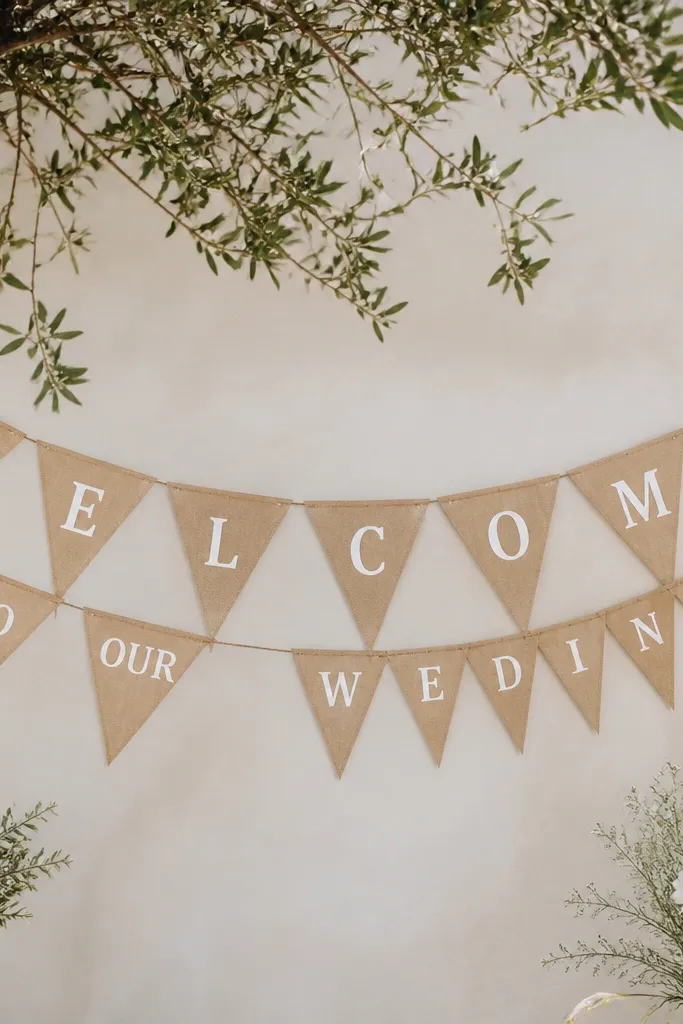 A kraft paper pennant banner with 7 triangle flags. Each triangle has crisp white vinyl text spelling "WELCOME" across the top line and "TO OUR WEDDING" below on alternating flags.