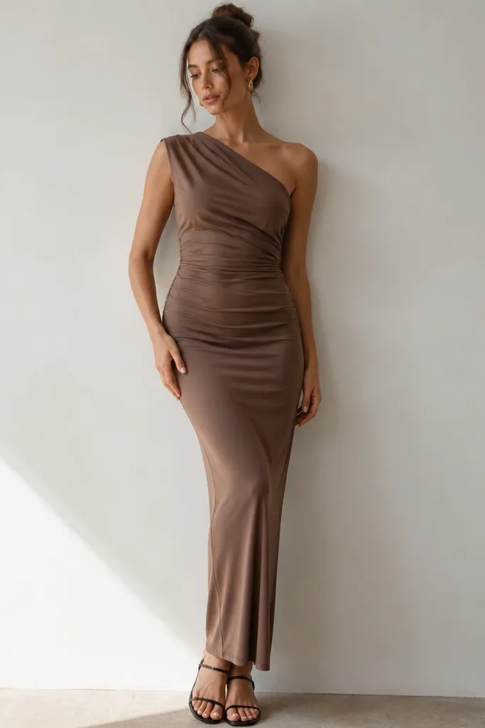A mocha brown knit dress with a one-shoulder neckline and a draped panel across the chest. The image shows a smooth, stretchy fabric and a simple black sandal with a thin strap.