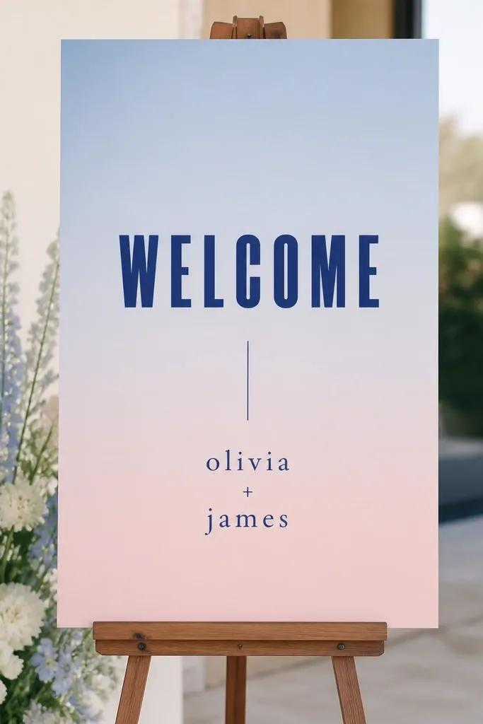 A 12x18 sign with a vertical pastel ombre background from powder blue to blush. Bold block letters spell "Welcome" in deep navy, with names in smaller lowercase.